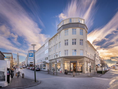 Picture of a corner building at Laugavegur and Skólavörðustígur. In the foreground are empty streets and parking signs.