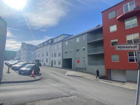Auð gata og hús. Nokkrum bílum lagt við götuna.