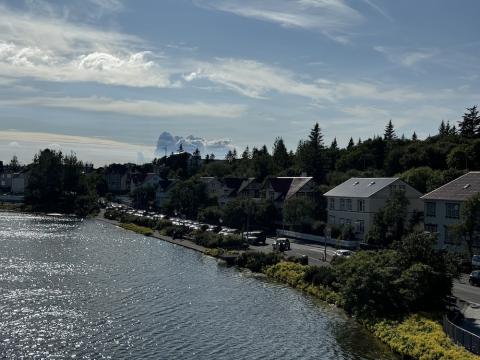 The pond, houses, vegetation, and eruption plume in the distance.
