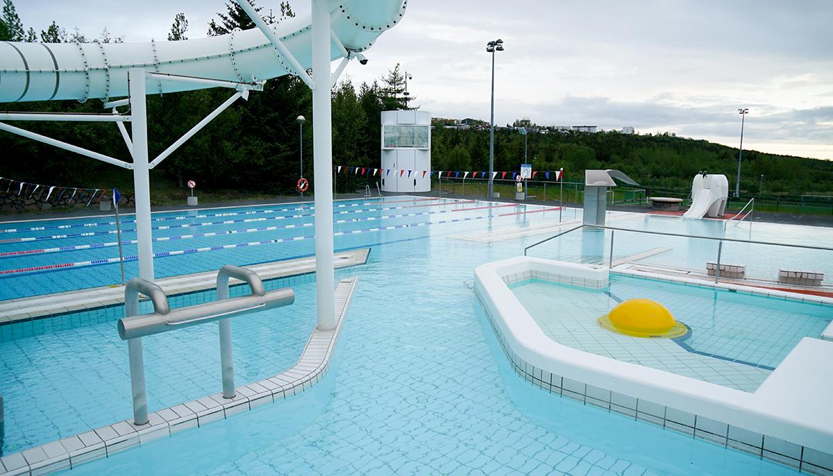 View across outdoor facilities at Árbæjarlaug toward Elliðaárdalur