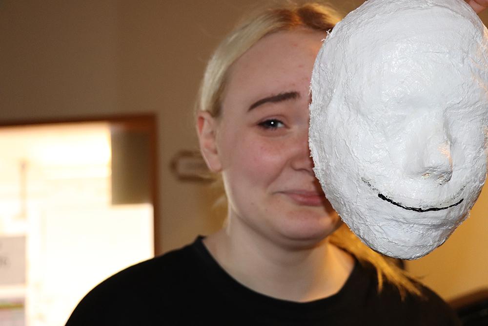 Grátandi stúlka sem tekur af sér hvíta pappamassa grímu.