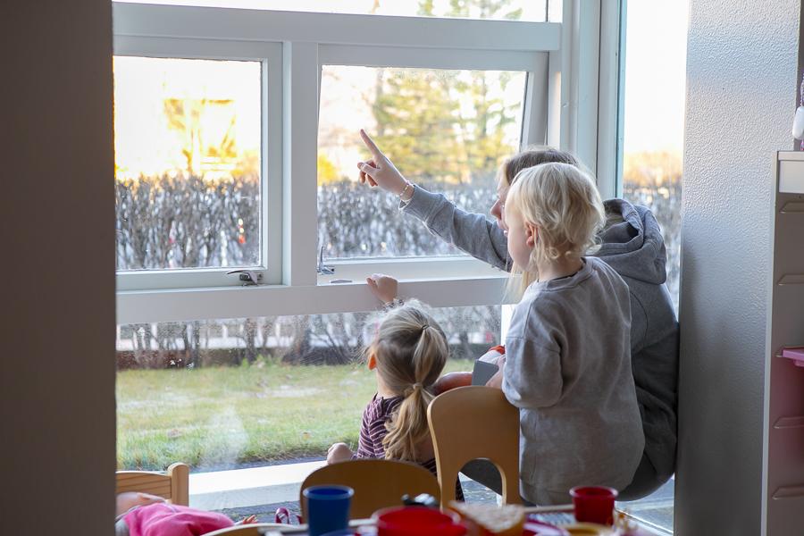 Börn að horfa út um glugga ásamt leikskólakennara