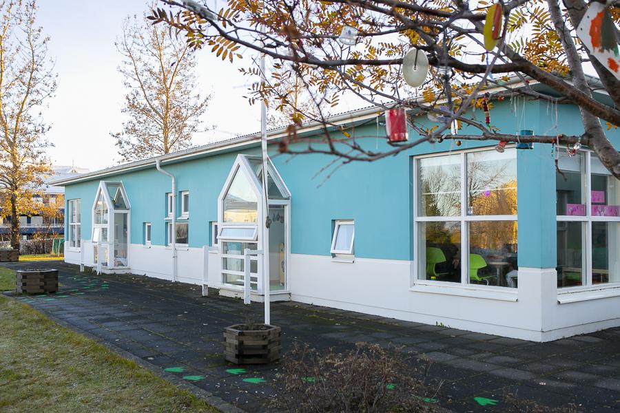 Hús leikskólans Brekkuborgar séð frá útisvæði. Laufblöð og greinar í forgrunni