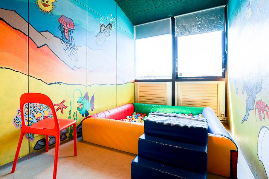 Multicolored ball pit, red chair and decorated wall.