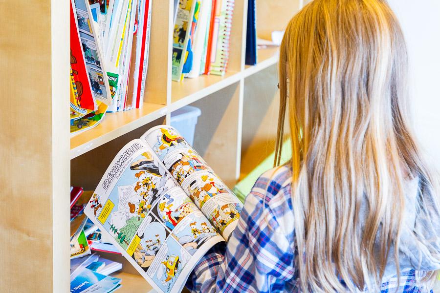 A child stands by a shelf reading a Donald Duck comic book. 