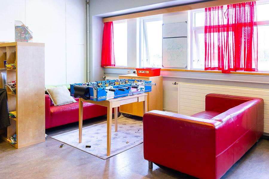 A room with red couches, red curtains, a shelf, and a foosball table.