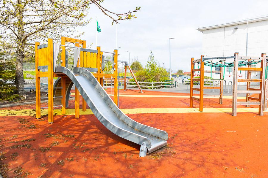 A slide and a jungle gym on a red surface.