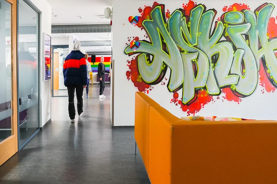 Wall artwork in front of an orange sofa. Young people in the hallways. 