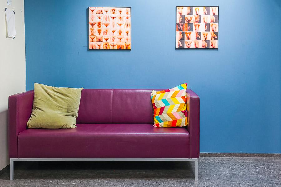 Purple sofa against a blue wall. Two pictures hang on the wall. 